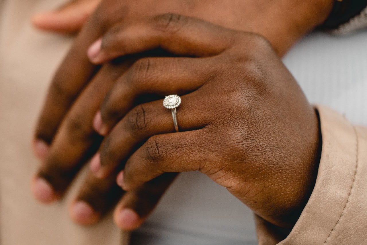Two hands holding, one of them wearing a silver, oval cut, diamond engagement ring