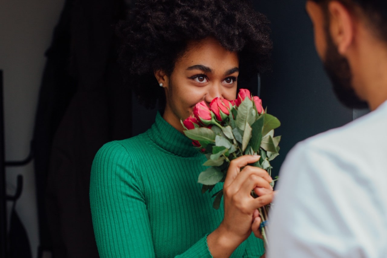 A woman getting picked up for a Valentine’s Day date is smelling the roses her date brought her