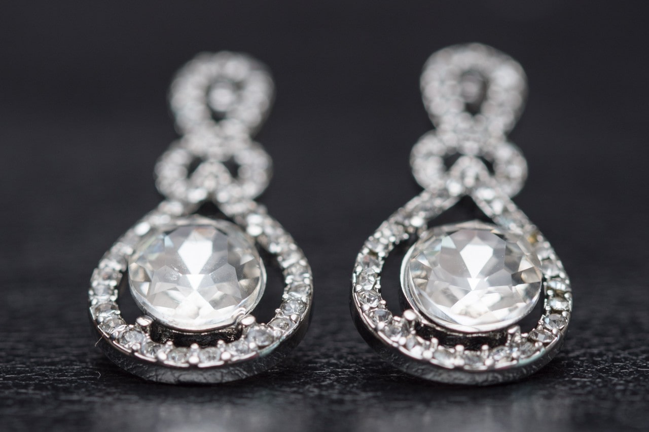 A pair of diamond drop earrings sit on a black wood background