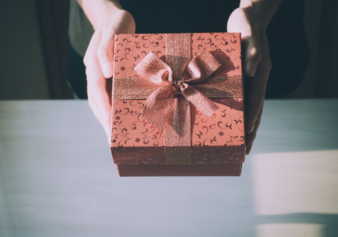 A woman presents a wrapped gift box with a sparkly bow during a coffee date with a friend to celebrate their birthday