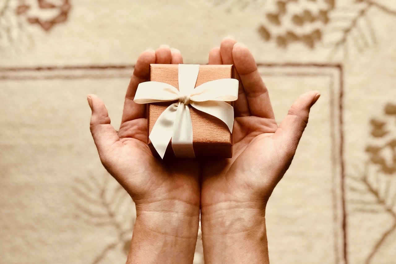 A golden gift box with a white ribbon sits in a man’s hands