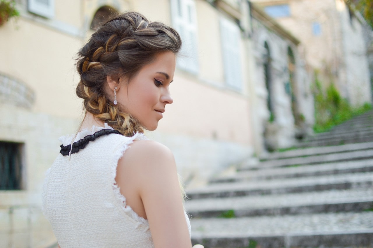 A woman with braided hair strolls through the city wearing diamond drop earrings