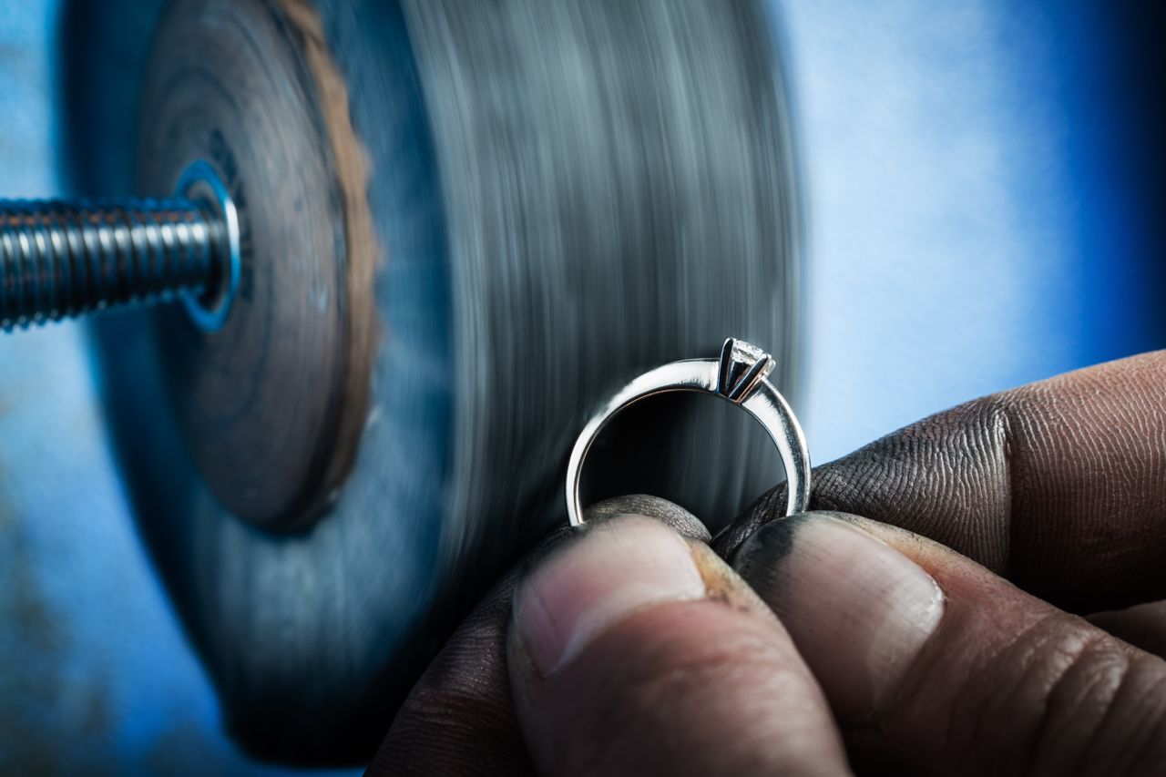 A jeweler grinding down a silver engagement ring with residue on their fingers.