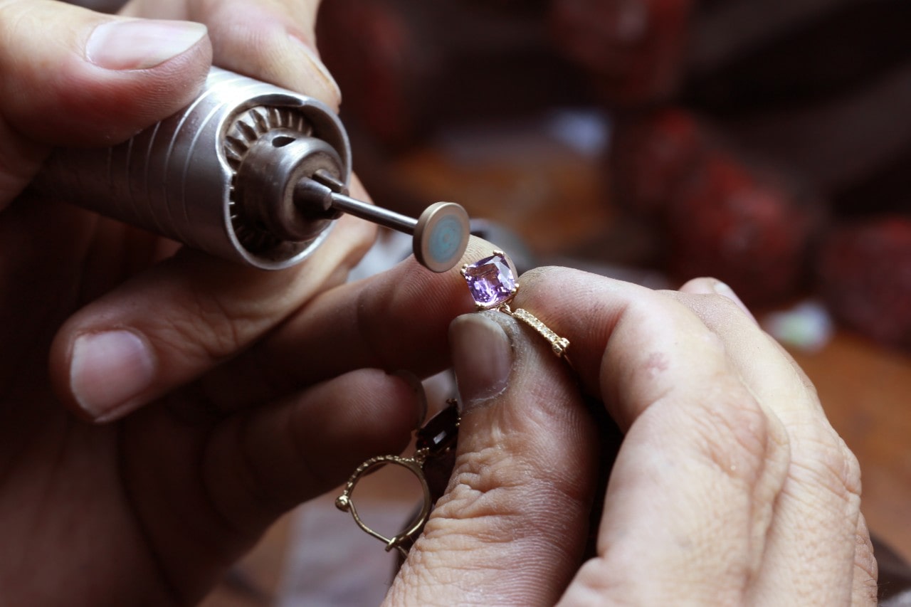 A jeweler polishing a purple gemstone on a gold hoop earring.