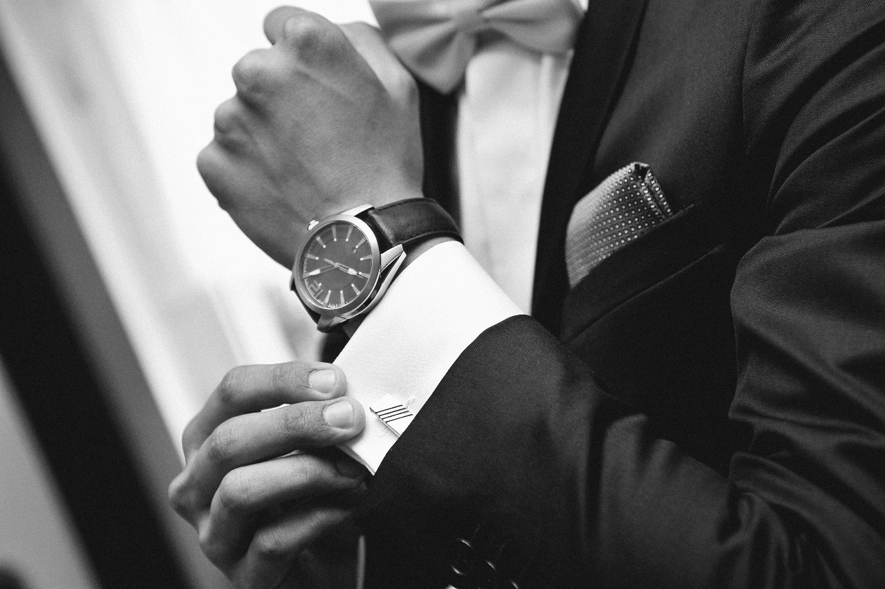 A black and white image of a man in a tux adjusting his cuff link, showcasing his luxury watch.