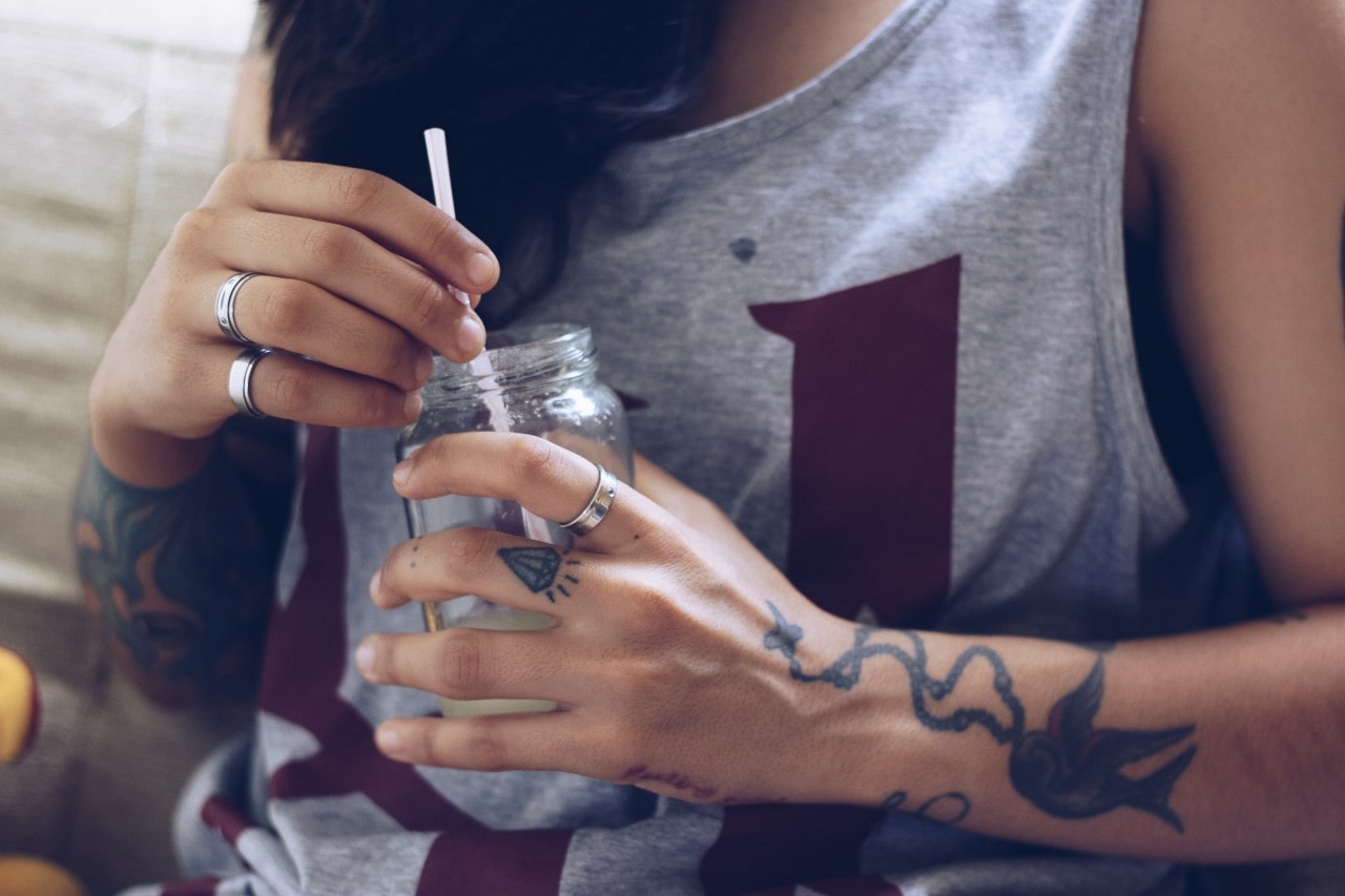 A woman wearing sterling silver rings sips a drink out of a mason jar.