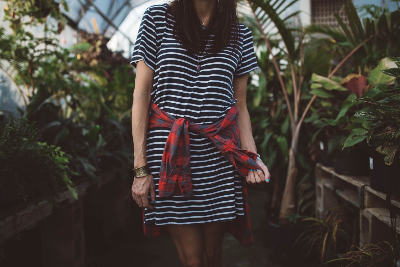 A woman wearing a dress with a flannel wrapped around her waist wears an elastic bracelet.