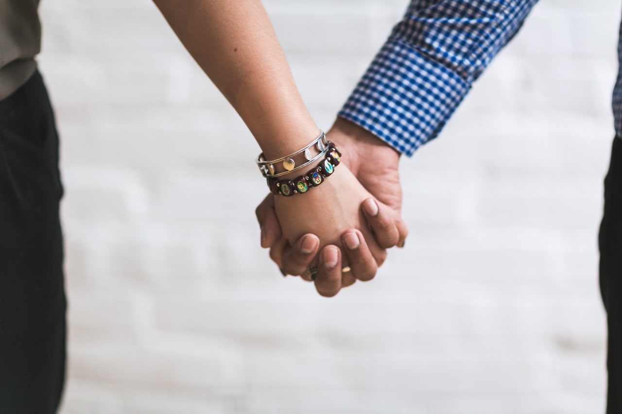 A couple holding hands, the woman wearing a silver bangle and a gemstone bracelet.