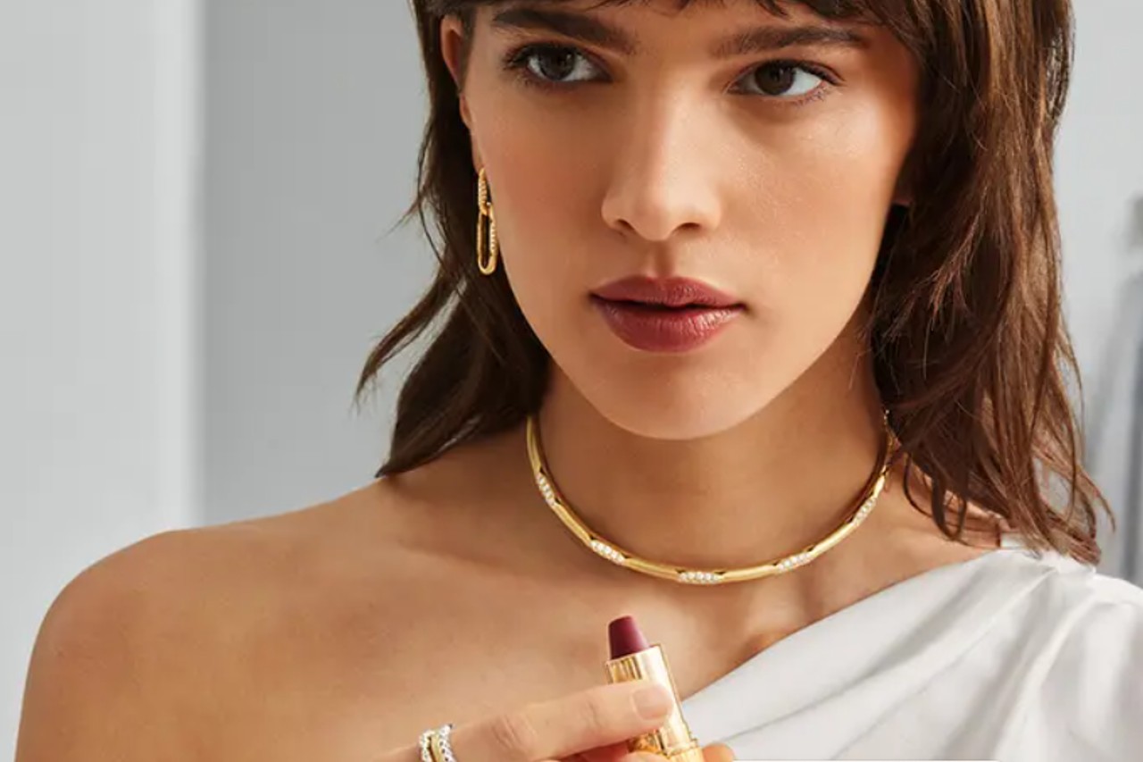 A woman wearing gold Tacori fashion jewelry and holding a tube of lipstick A woman wearing gold Tacori fashion jewelry and holding a tube of lipstick